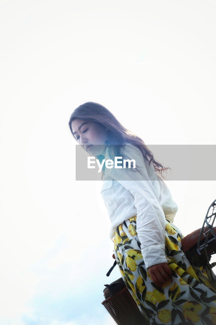 Low angle view of young woman standing against clear sky