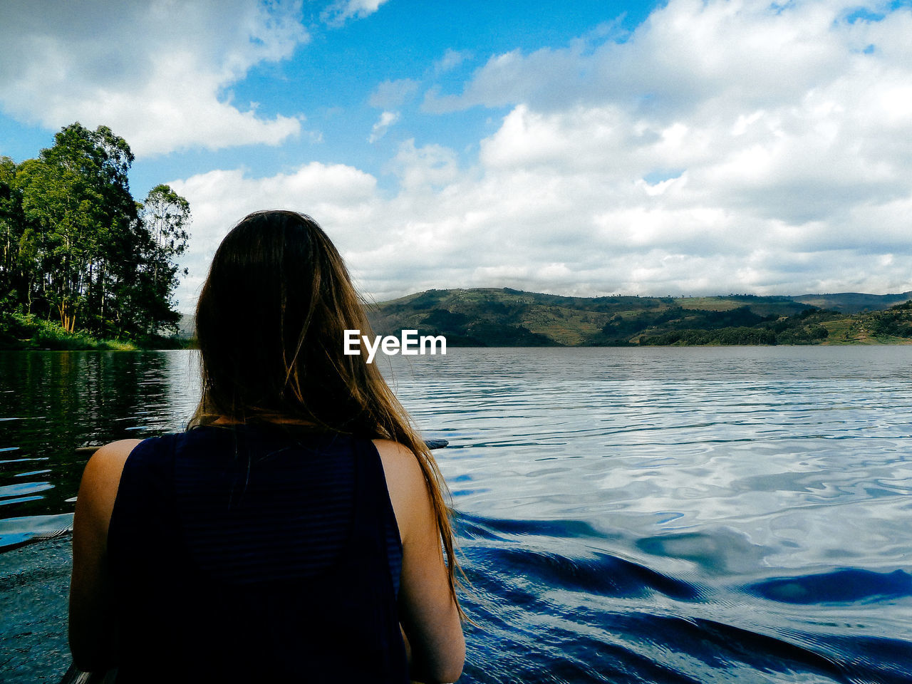 Rear view of woman sitting on boat in lake against cloudy sky