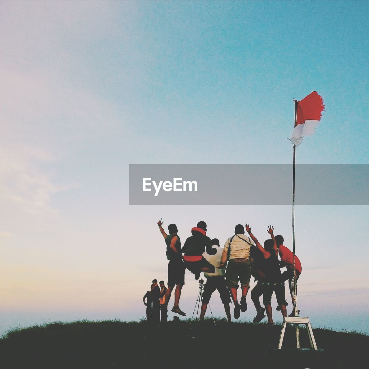 Low angle view of friends jumping on hill by indonesian flag at sunset