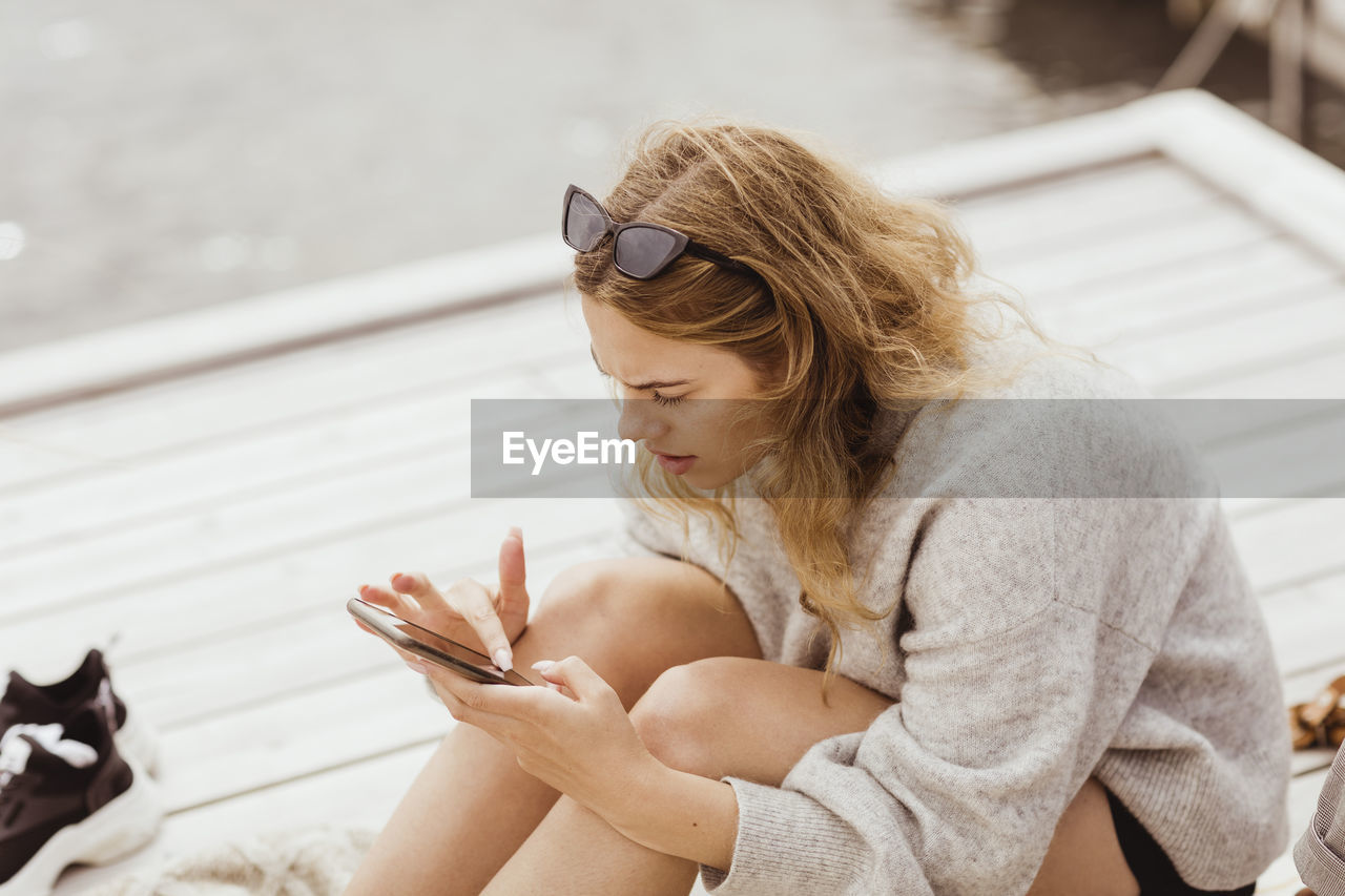 YOUNG WOMAN LOOKING DOWN WHILE SITTING ON OUTDOORS