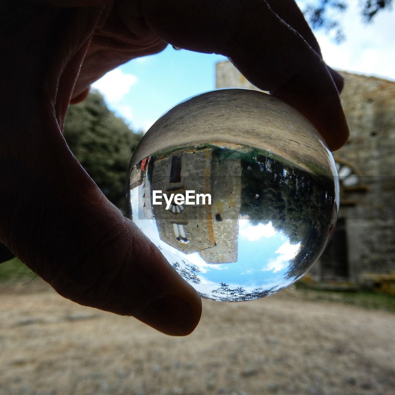 Cropped hand holding crystal ball with reflection of built structure