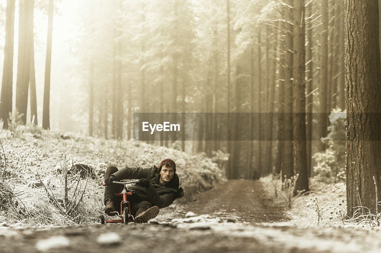Young man riding small bicycle on dirt road in forest during winter