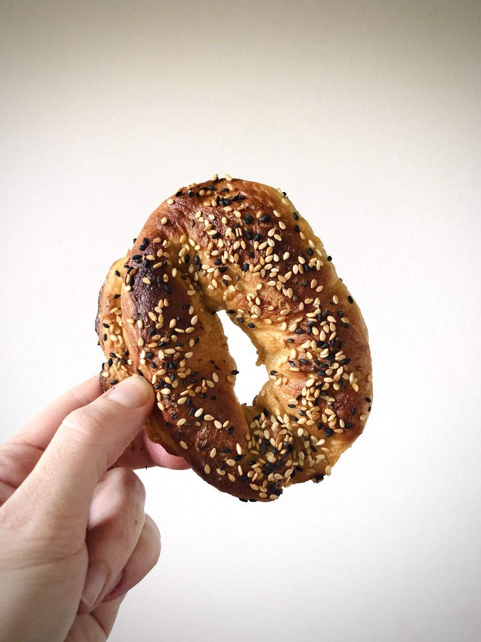 Close-up of hand holding montreal style sesame bagel against white background