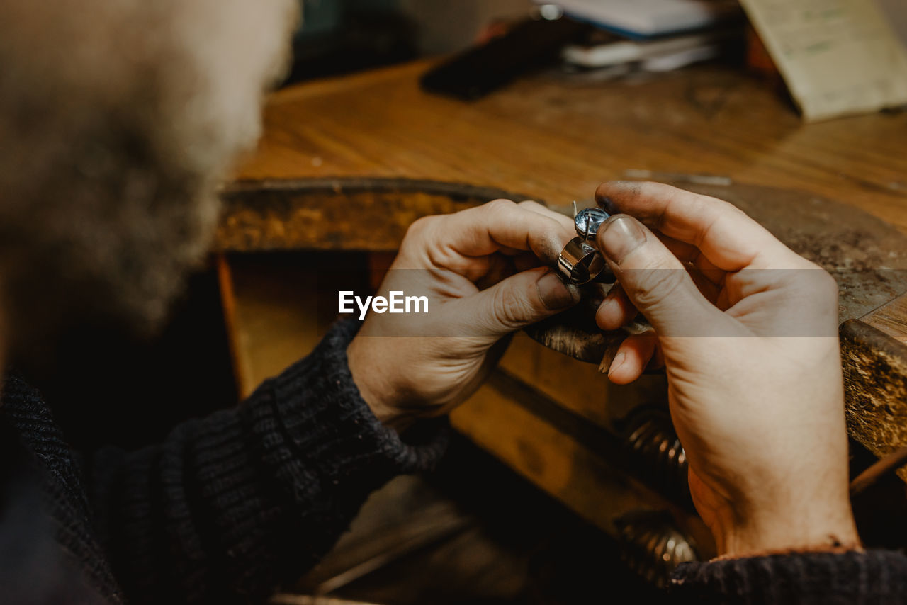 Anonymous jeweler holding unfinished ring in dirty hands and checking quality in workshop