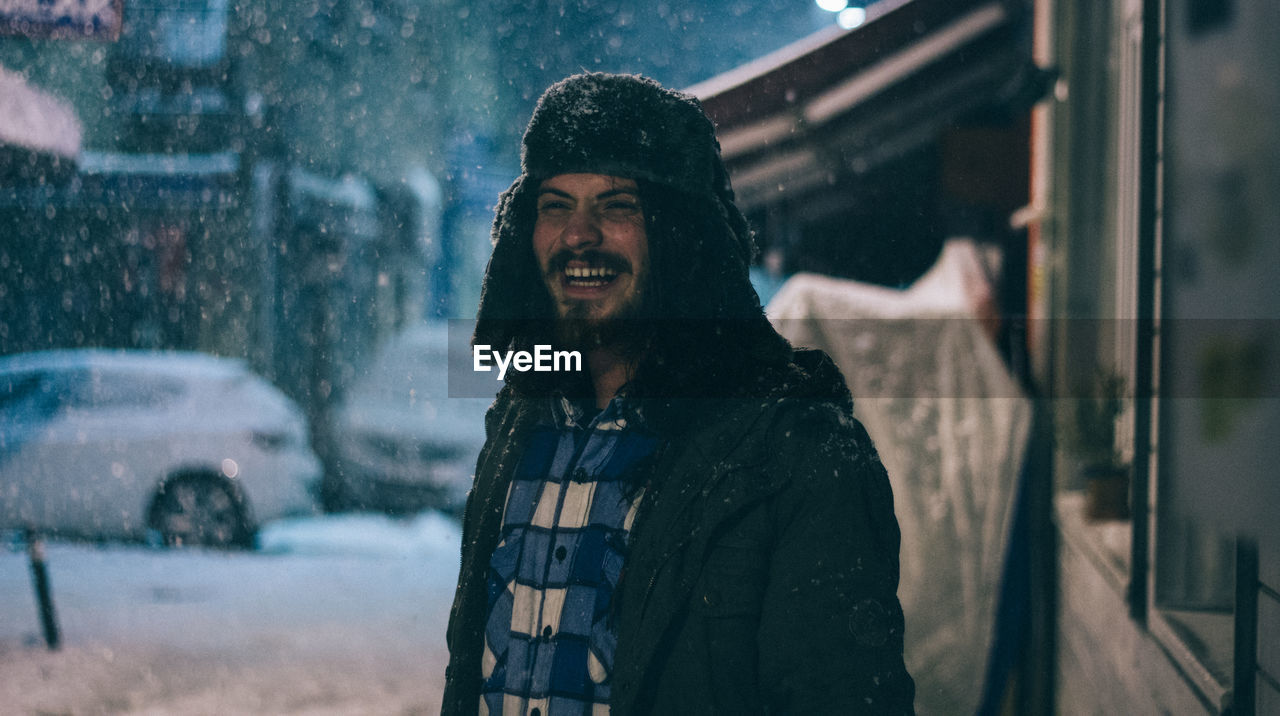 Young man smiling on street while snowing