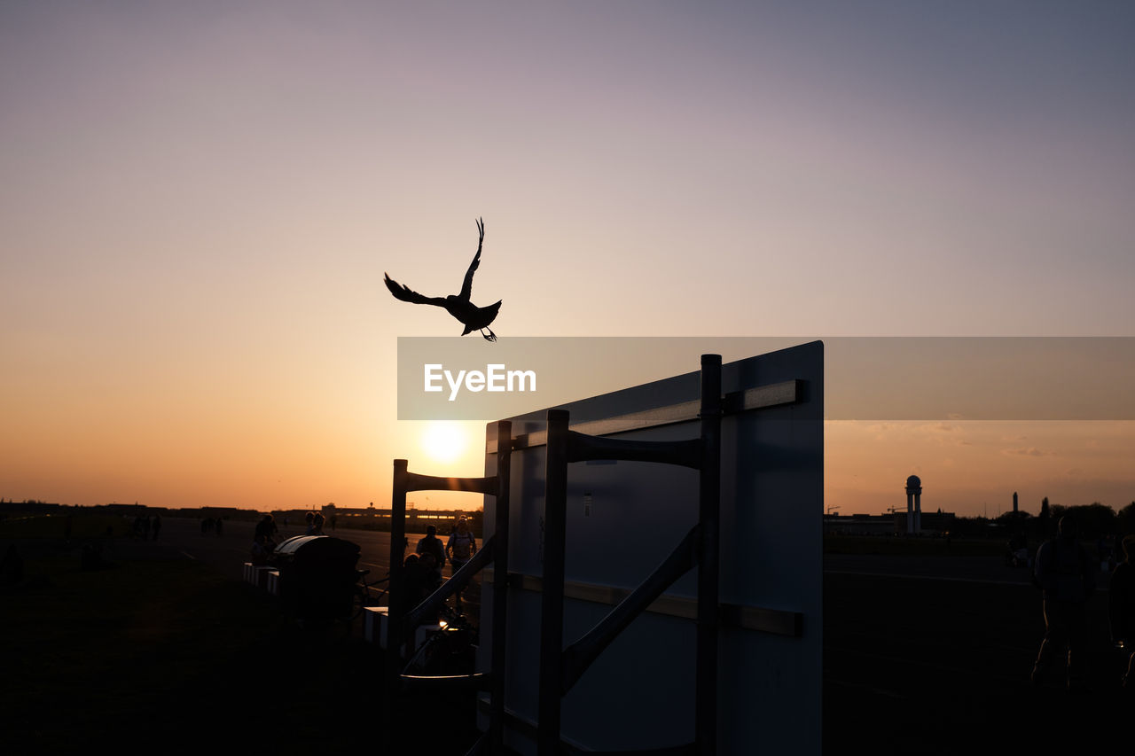 Silhouette bird flying over upside down table against sky during sunset