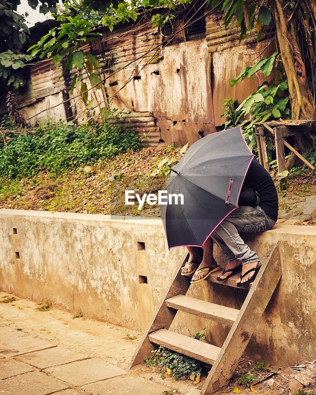 Couple on retaining wall hiding under umbrella