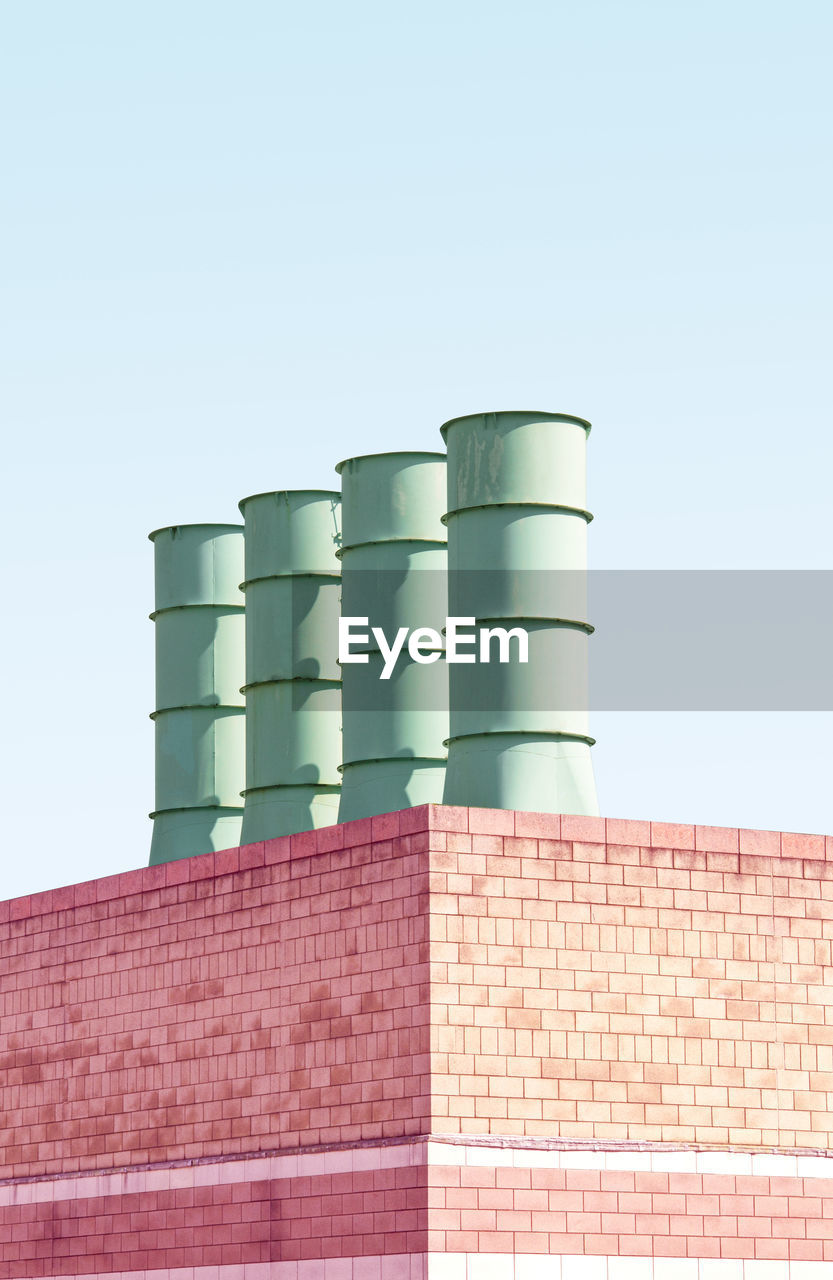 Low angle view of smoke stacks on building against clear sky
