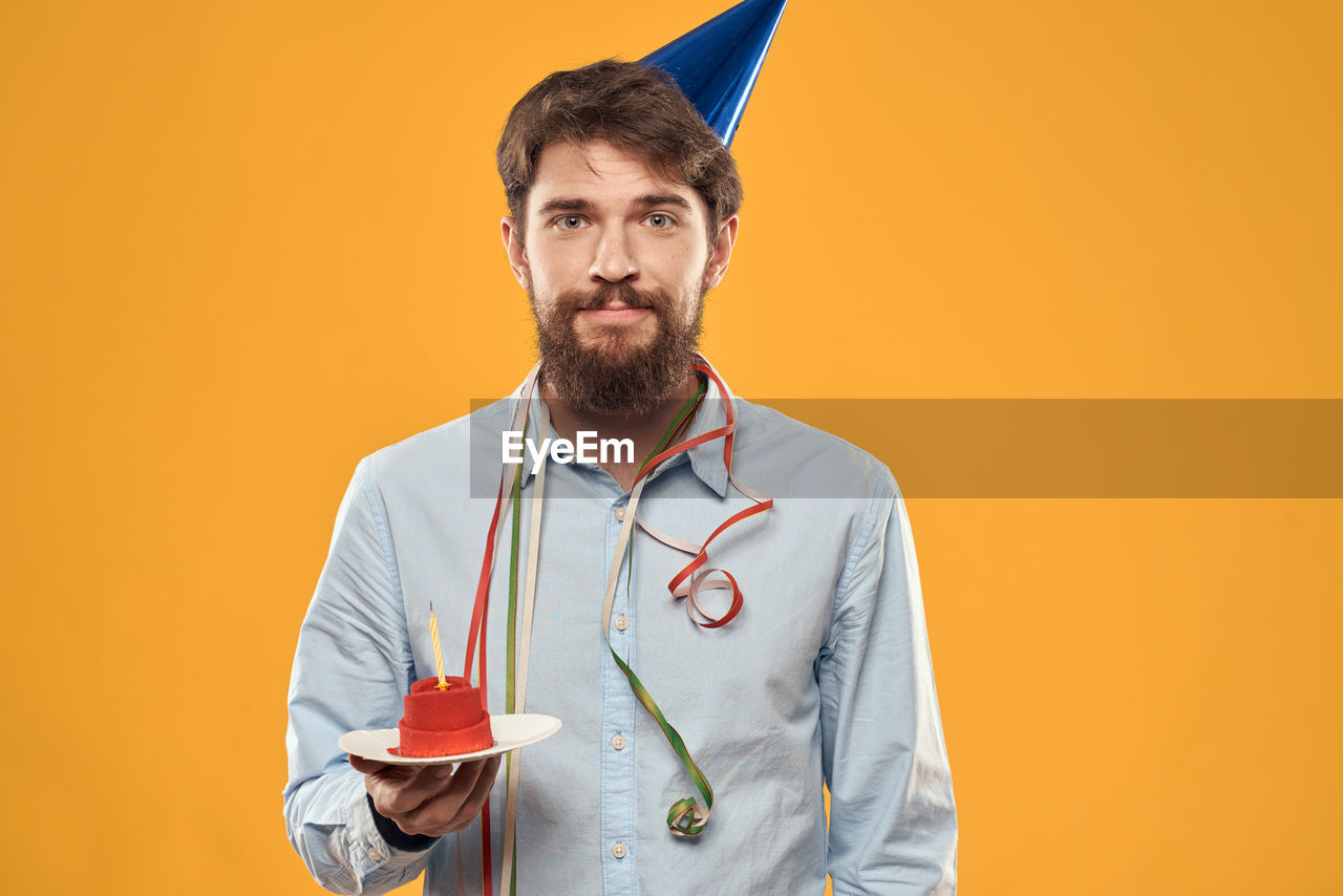 beard, facial hair, one person, colored background, portrait, adult, studio shot, looking at camera, stethoscope, indoors, men, medical instrument, yellow, person, yellow background, waist up, young adult, copy space, clothing, occupation, standing, front view, smiling, medical supplies, emotion, happiness, holding, orange color, brown hair, medical equipment, doctor