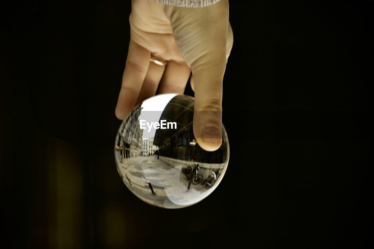 Cropped image of person holding crystal ball against black background