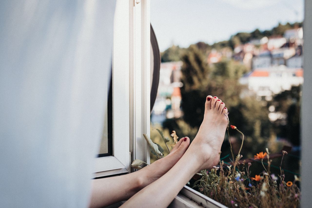 Low section of woman relaxing with legs on window at home
