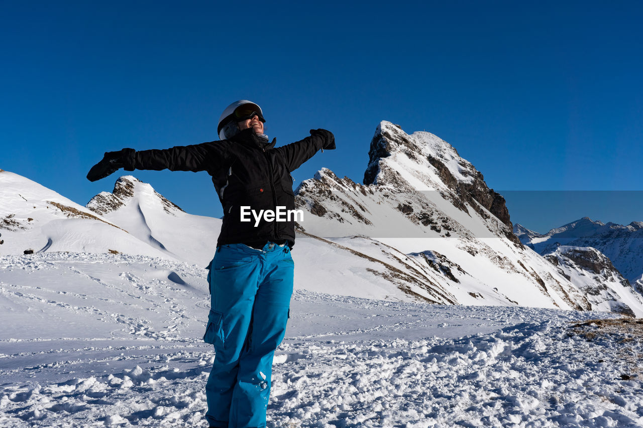 Woman standing by snowcapped mountain against blue sky