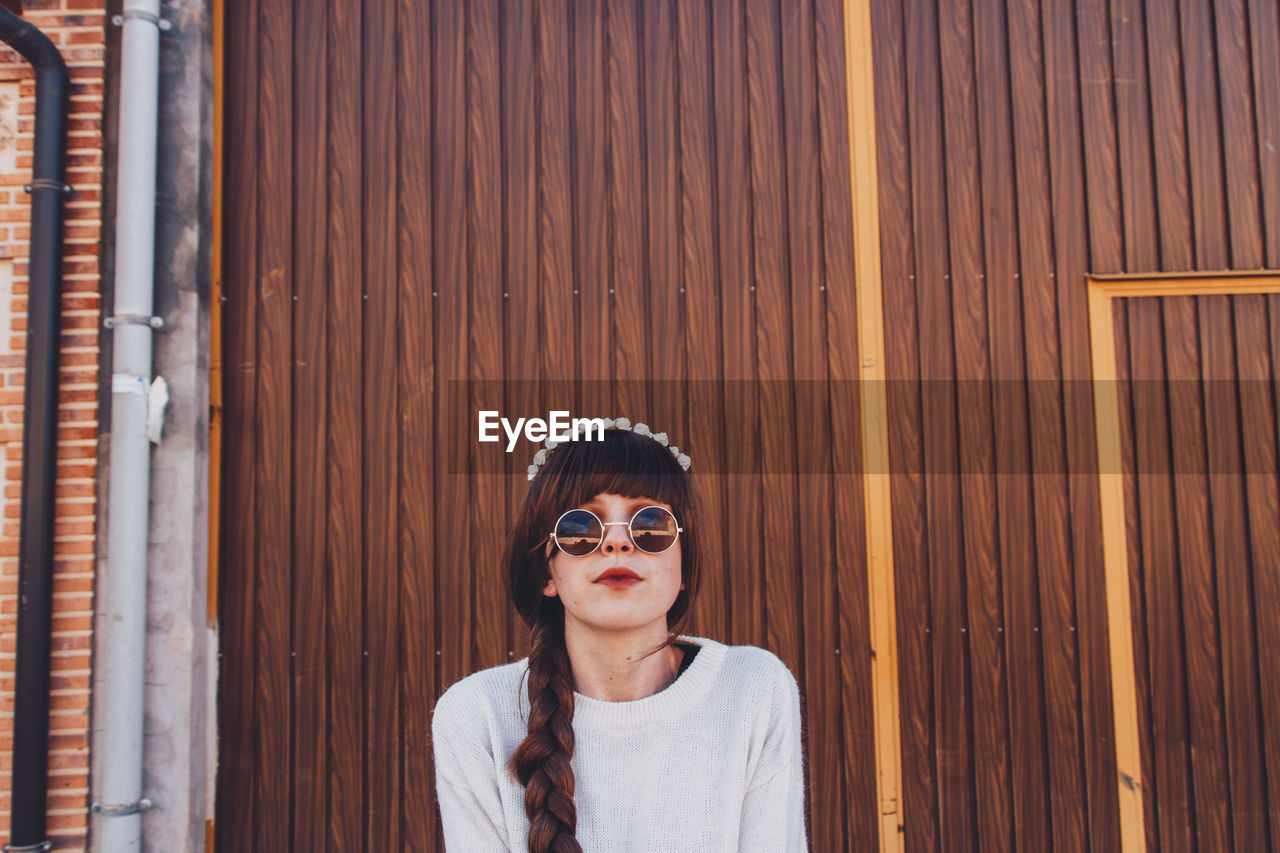 Portrait of woman wearing sunglasses while standing against wall