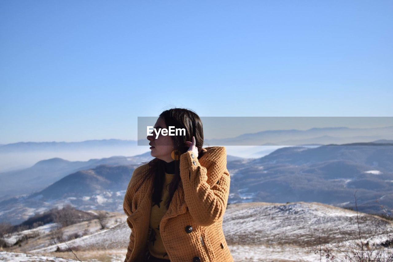 Young woman looking away against blue sky at mountains