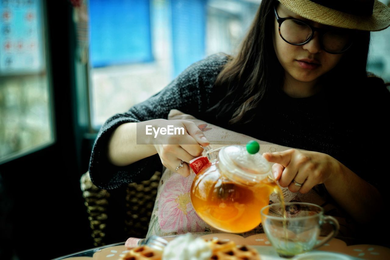 Young woman pouring tea from pot in cup