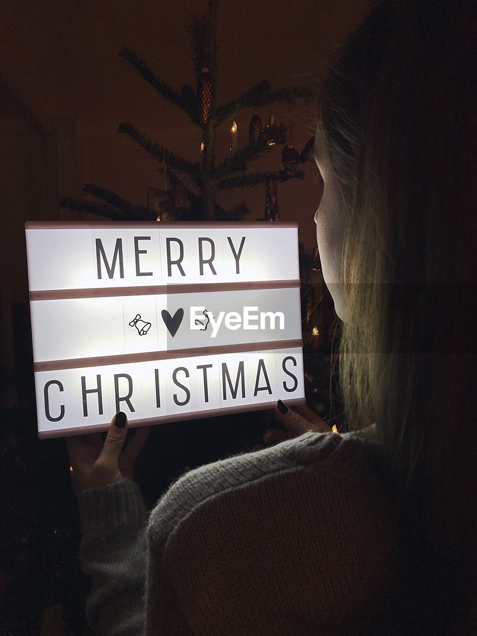 Rear view of woman holding illuminated lightbox with text