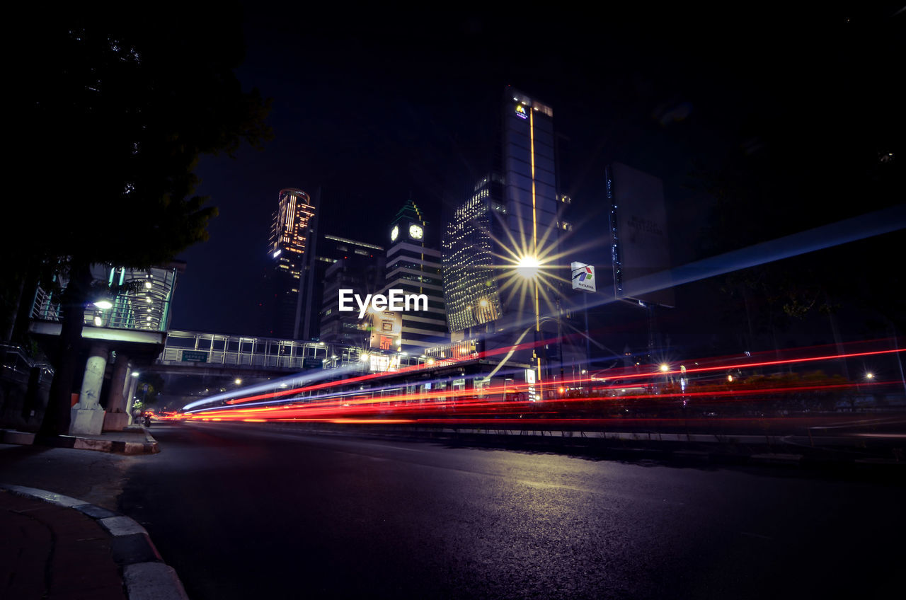 LIGHT TRAILS ON ROAD ALONG ILLUMINATED STREET LIGHTS AT NIGHT