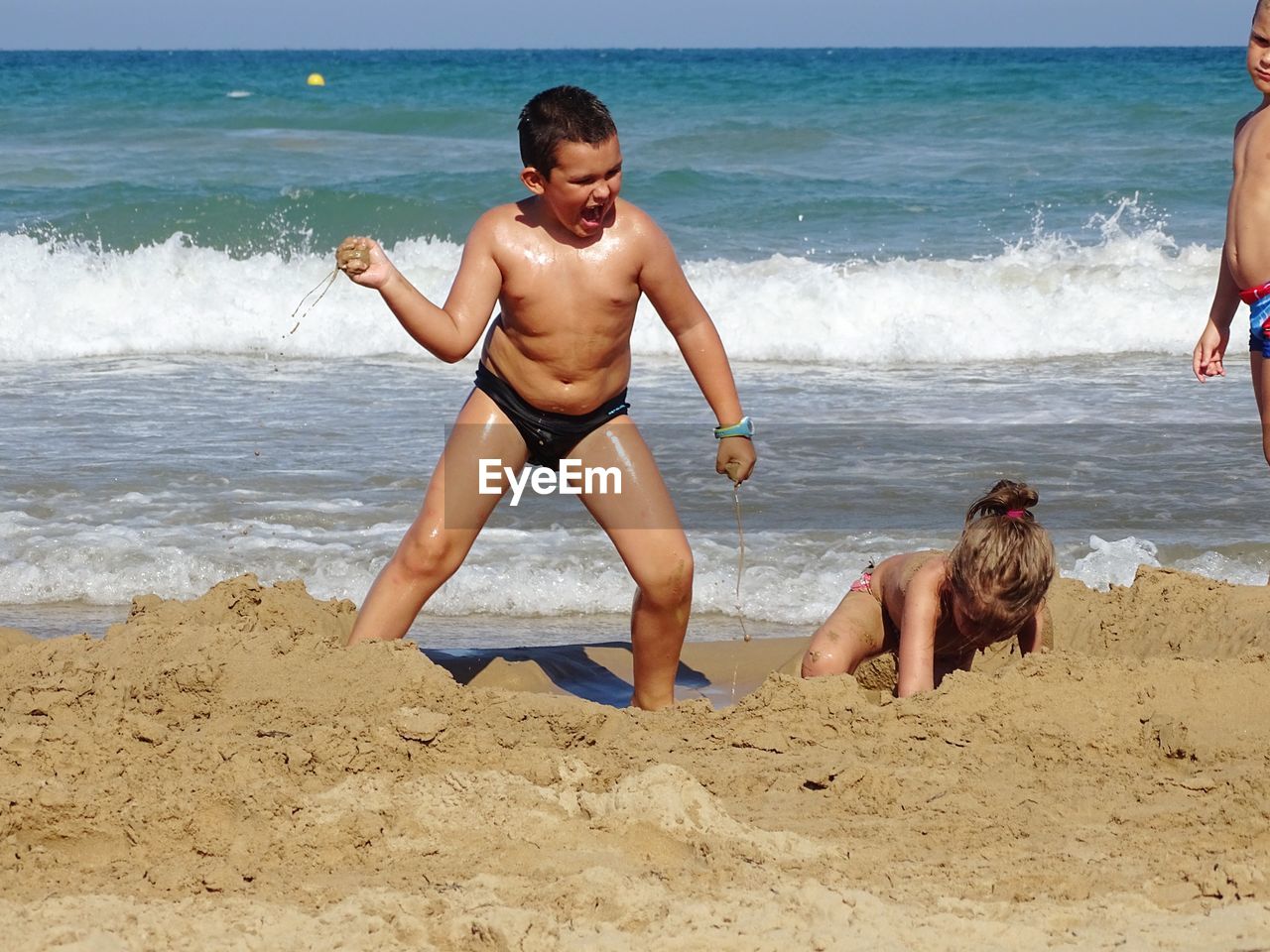 Shirtless boy throwing sand on sister at beach