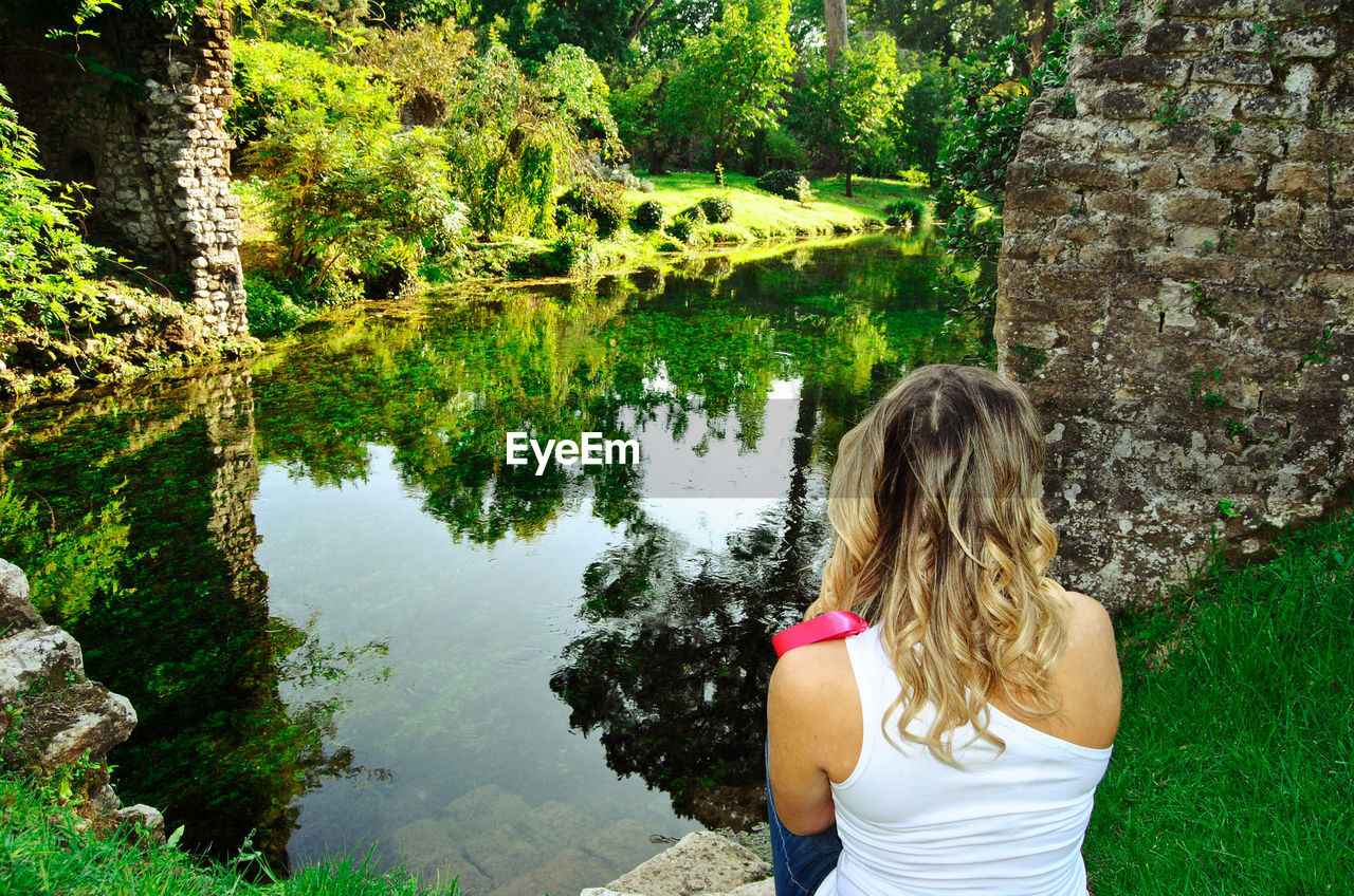 Garden of ninfa - rear view of blonde woman looking at the river