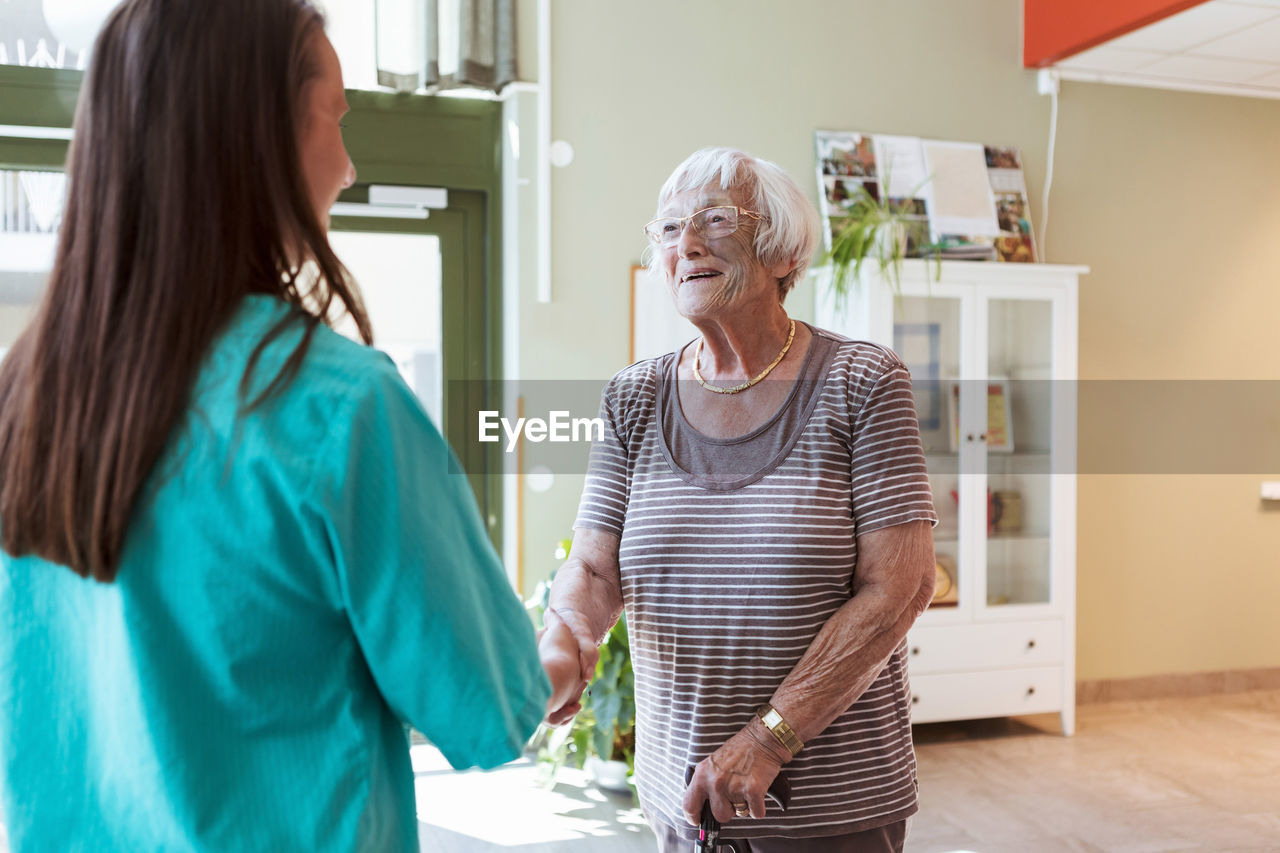 Smiling elderly woman shaking hands with nurse at nursing home