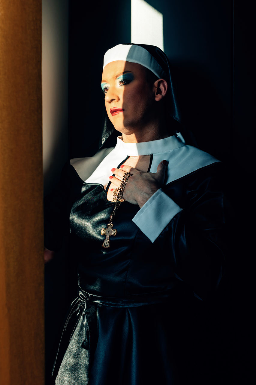 Cross dressing drag queen performing a praying catholic nun illuminated by a ray of light