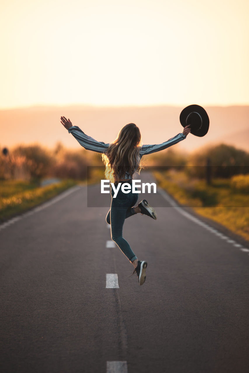 full length of woman exercising with arms raised standing on road