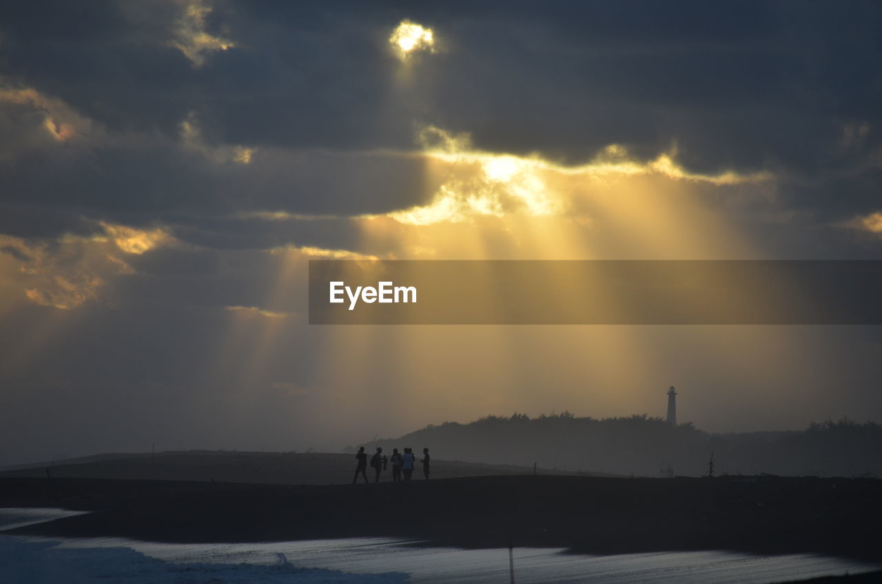People standing at beach against cloudy sky during sunset