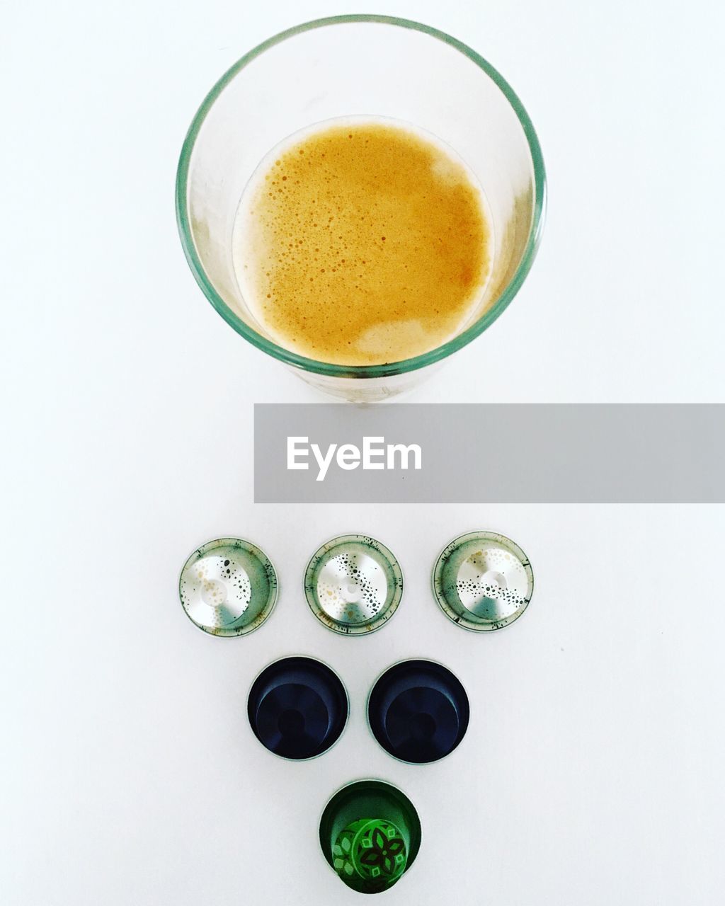 Directly above shot of coffee capsules and drinking glass against white background