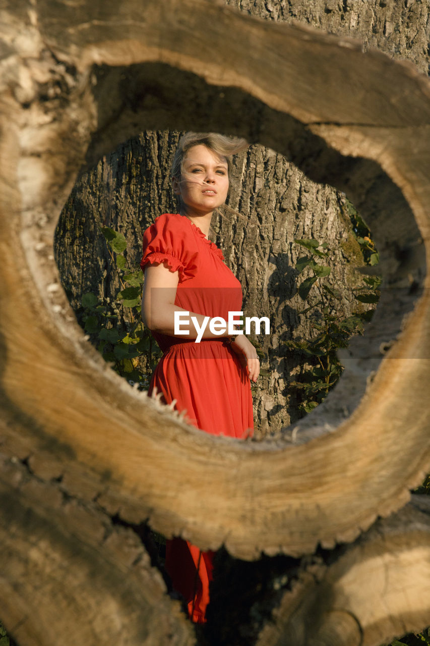 Portrait of smiling young woman against tree trunk