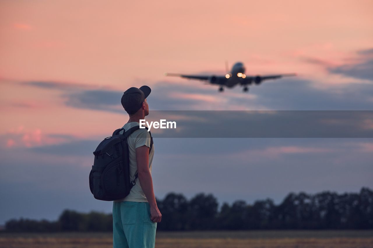 Rear view of man looking at airplane against sky during sunset