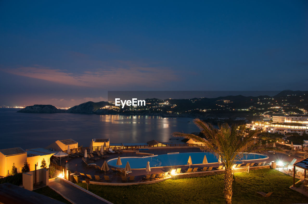 Illuminated tourist resort by sea against sky at dusk