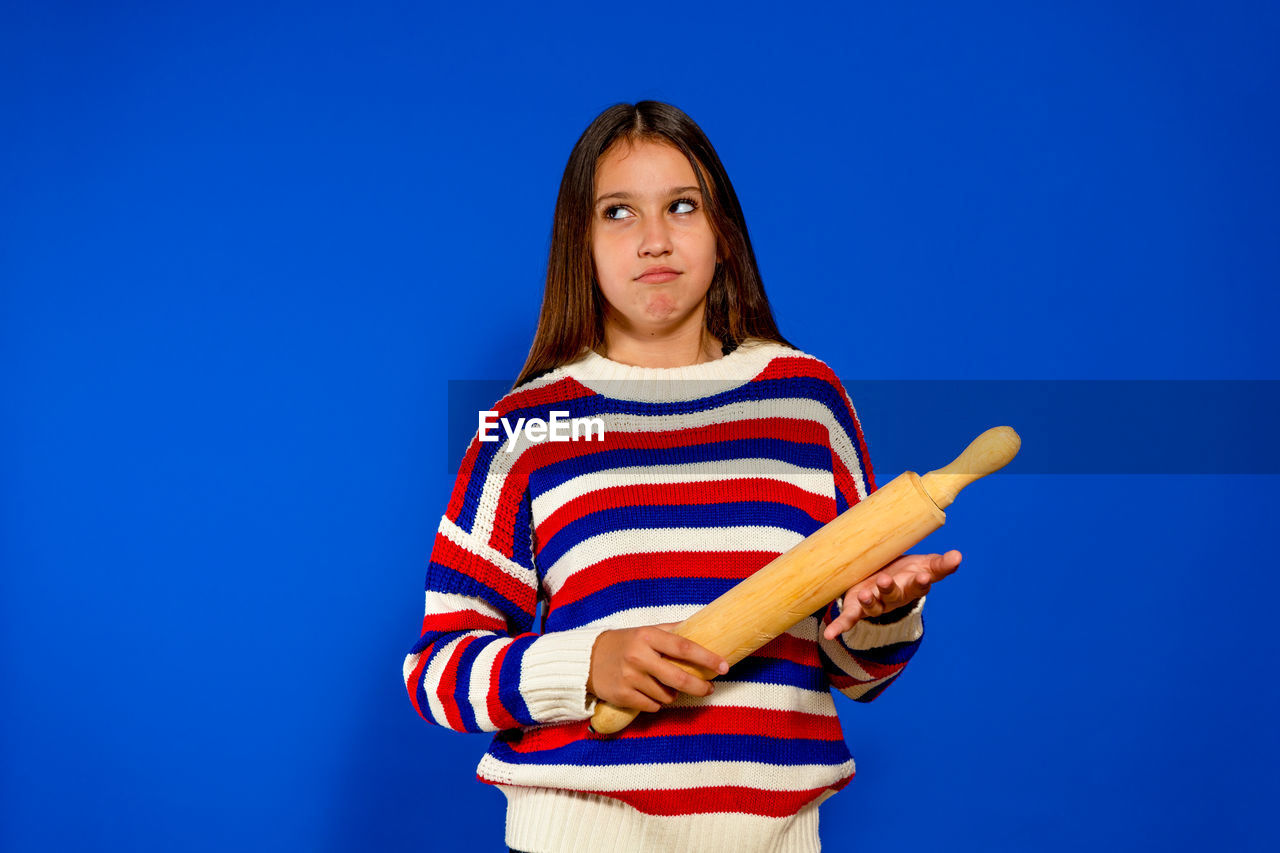 blue, striped, one person, studio shot, colored background, blue background, portrait, looking at camera, women, waist up, copy space, person, casual clothing, young adult, standing, adult, emotion, indoors, child, front view, clothing, photo shoot, childhood, holding, looking, hairstyle, female, long hair, brown hair, three quarter length