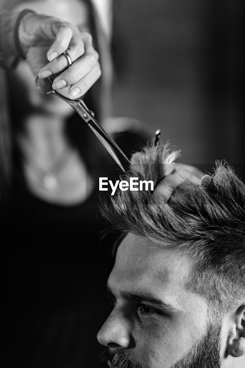 Close-up of woman cutting man hair at shop