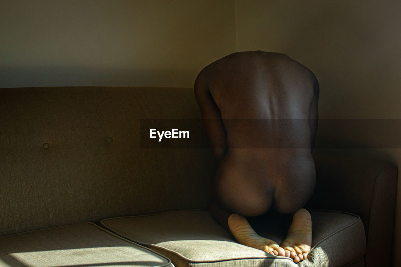 Naked man sitting on sofa at home