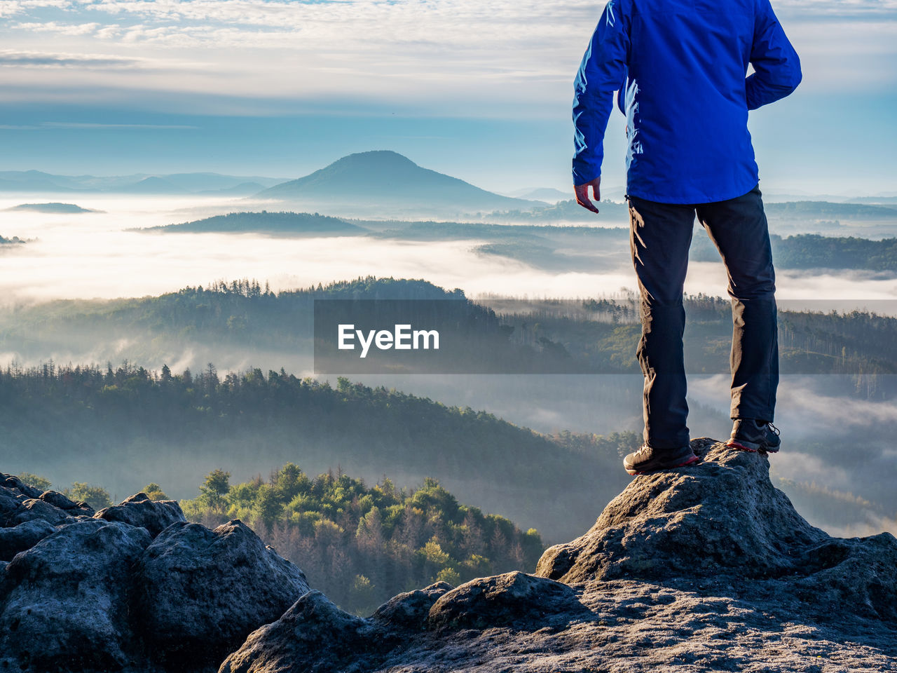 Man watch thick mist in valley from rocky view point in mountains. hiker climbed up alone 