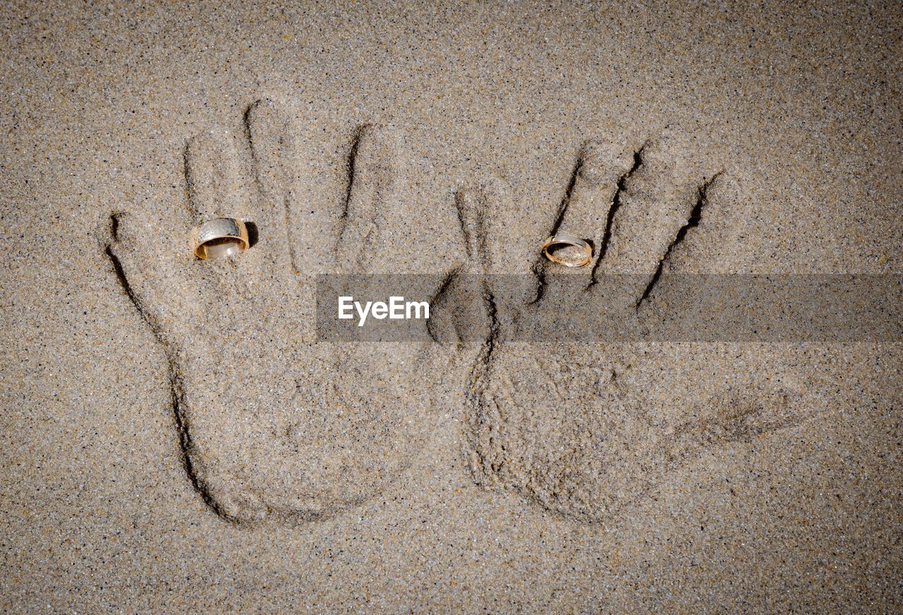 Directly above shot of wedding rings on hands in sand