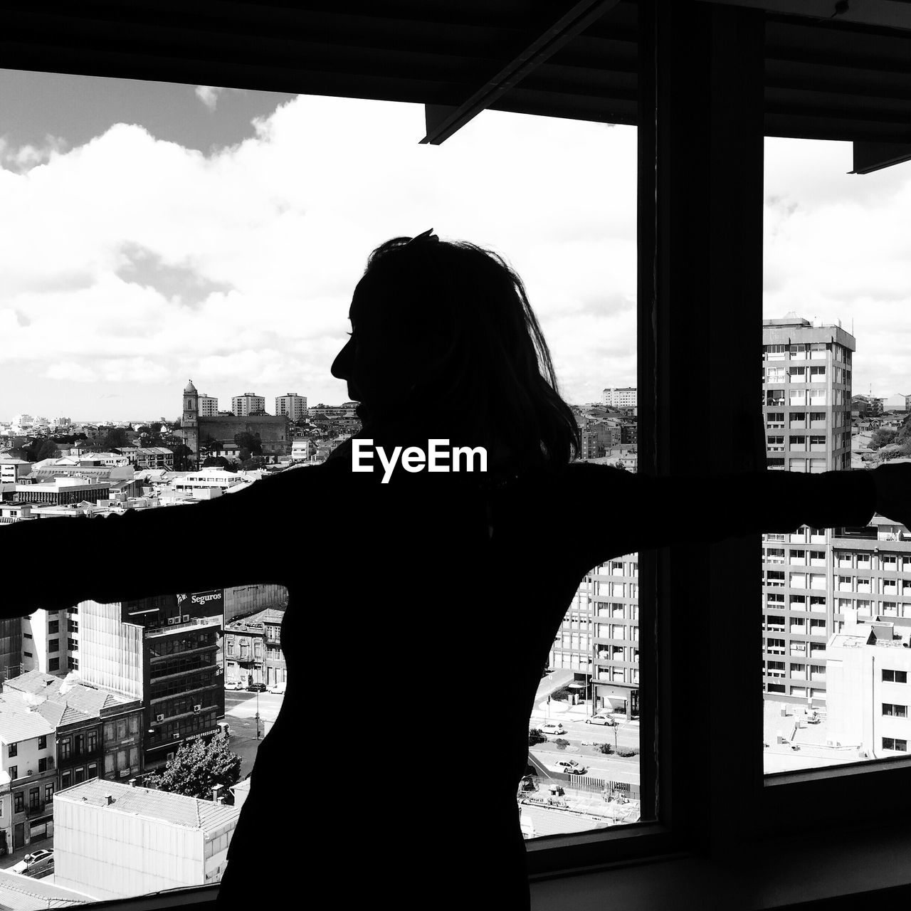 Rear view of person looking at cityscape against sky seen through window