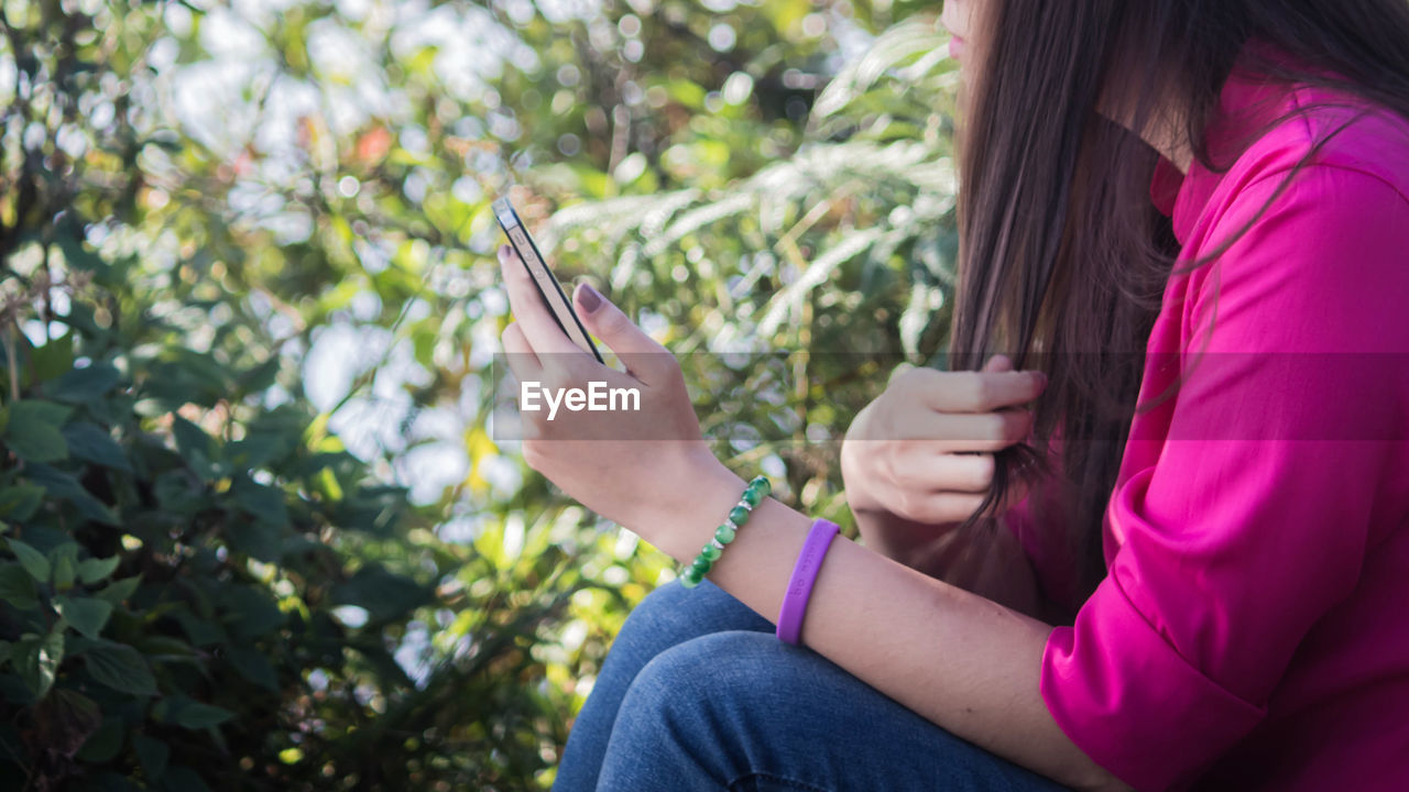 CLOSE-UP OF YOUNG WOMAN HOLDING SMART PHONE OUTDOORS