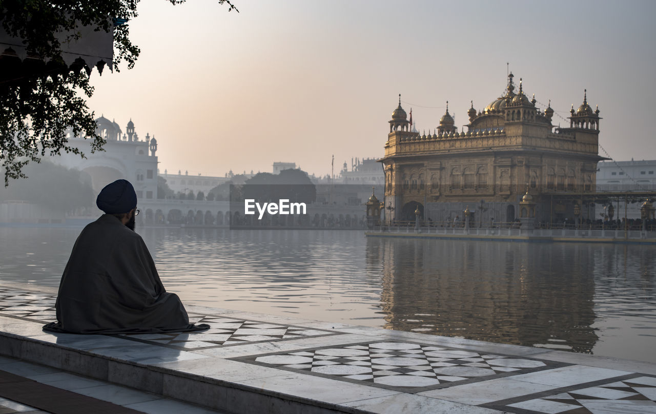 Man looking at golden temple against sky during sunrise