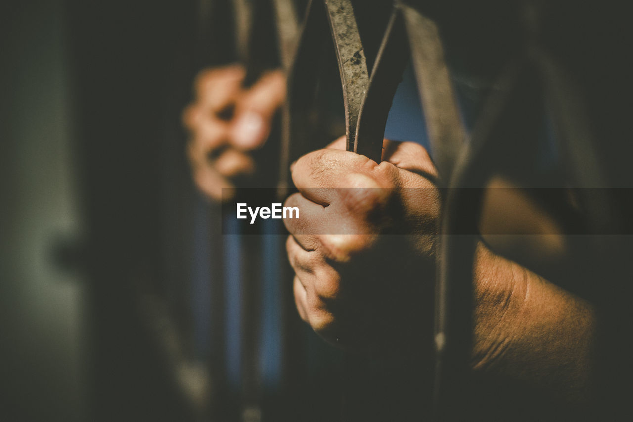 Cropped hands of male prisoner holding prison bars