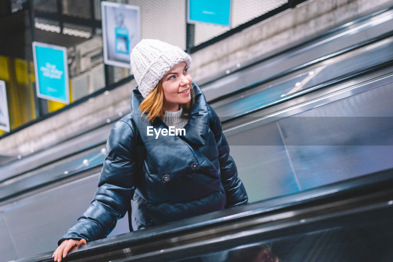 Portrait of smiling woman standing on escalator during winter