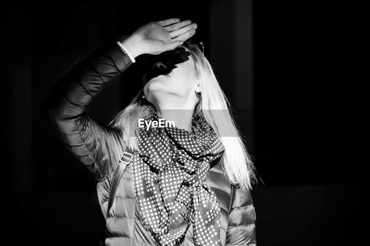 Woman shielding eyes while standing against black background
