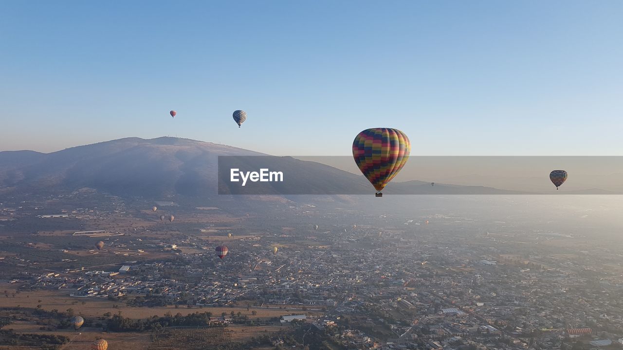 Hot air balloons flying over landscape against clear sky
