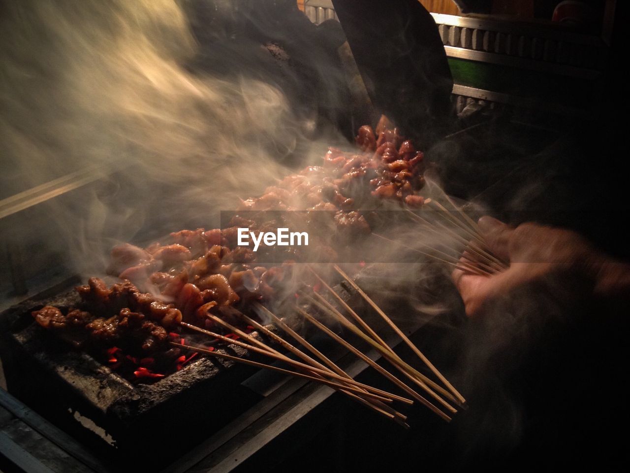 Cropped hand grilling chicken satay on barbecue grill