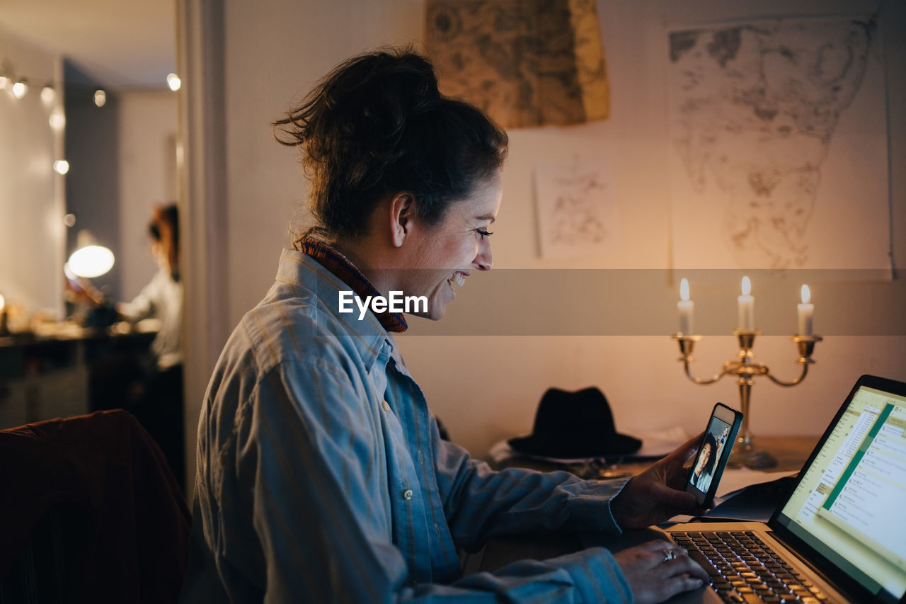 Smiling female engineer video conferencing on mobile phone while using laptop at desk