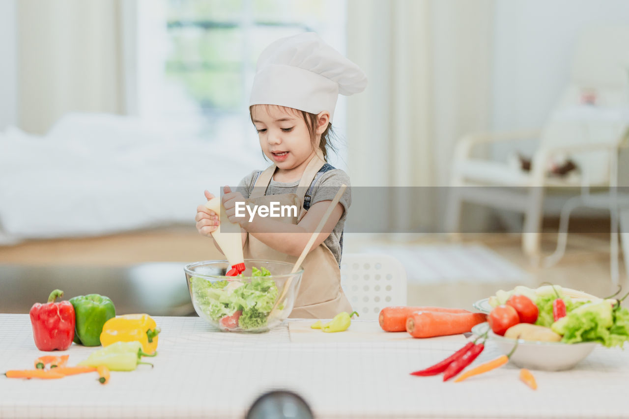 Sweet little cute girl is learning how to make a salad, in the home kitchen, family concept.
