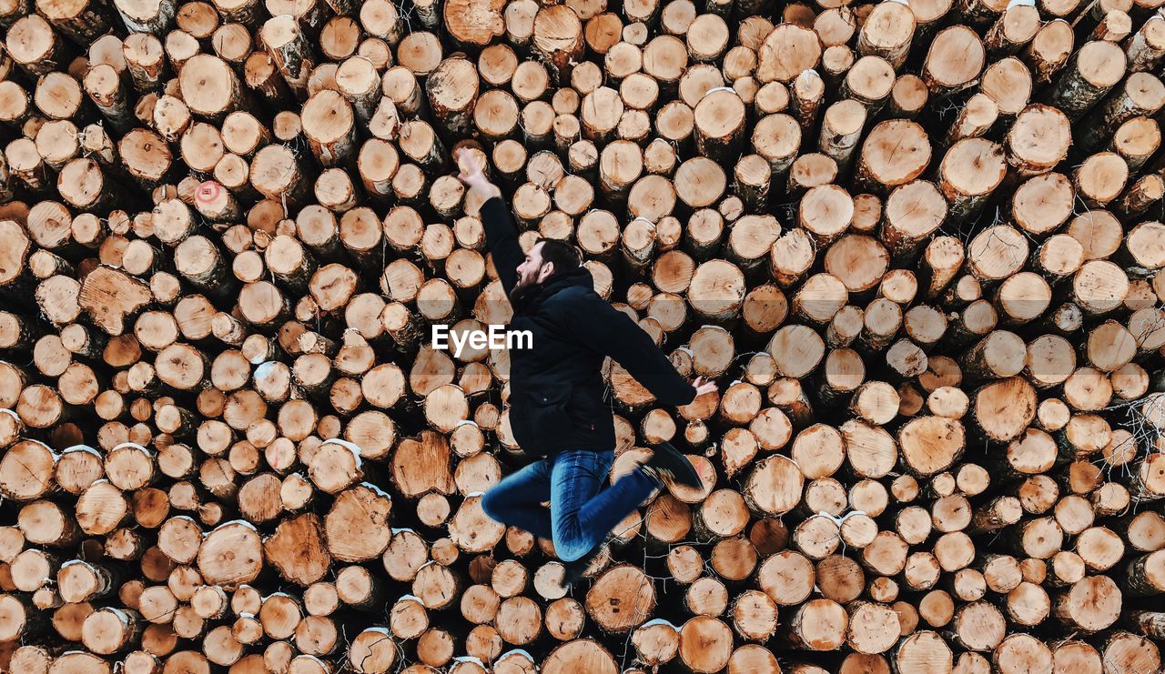 Side view of mid adult man jumping against logs