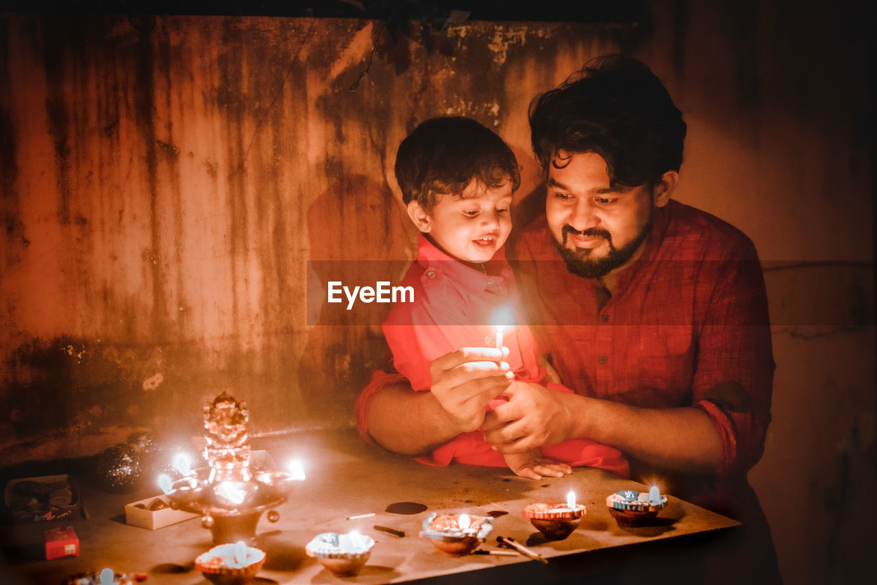 Father and son lighting diyas at night
