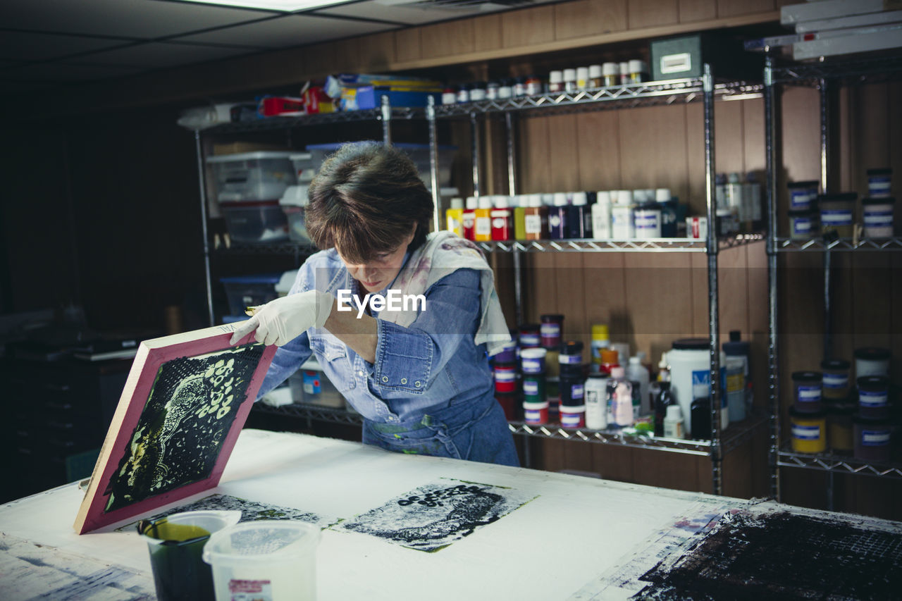 Craftswoman examining ink prints on workbench at workshop
