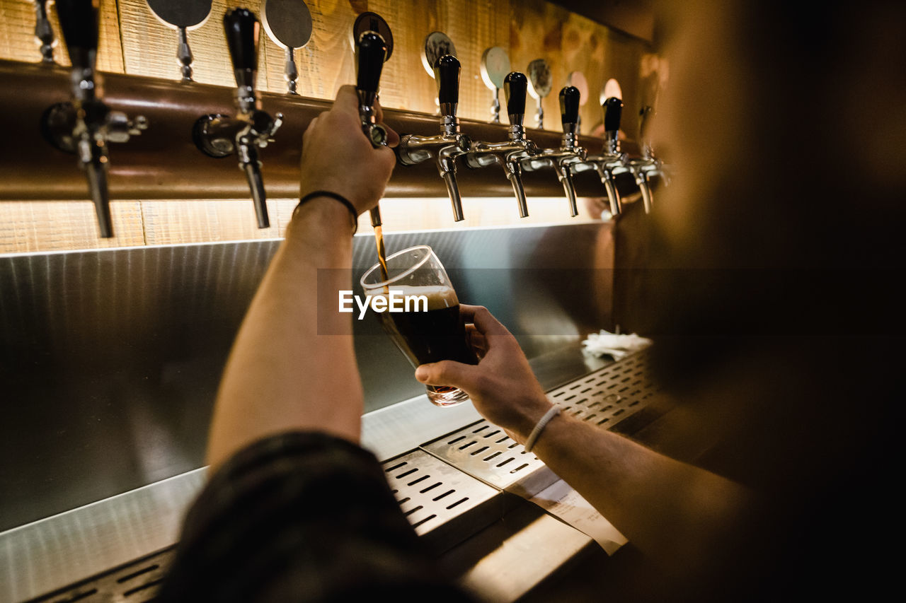 Cropped hands of man pouring beer from tap in glass